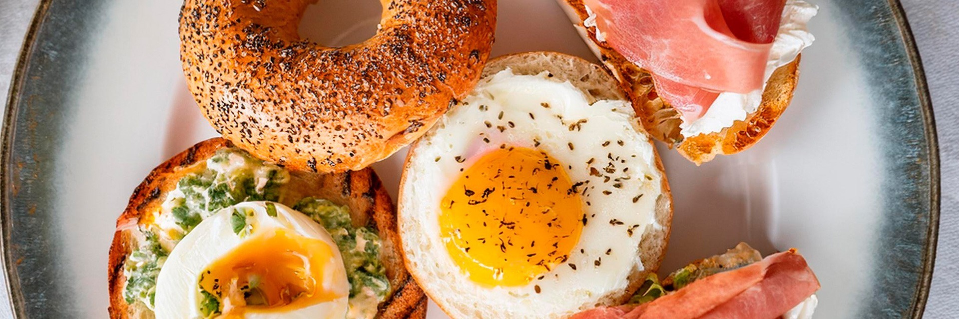 Bagel gourmet para el desayuno con salchicha, huevo frito y queso fundido, servido recién hecho en Roatan Provision.
