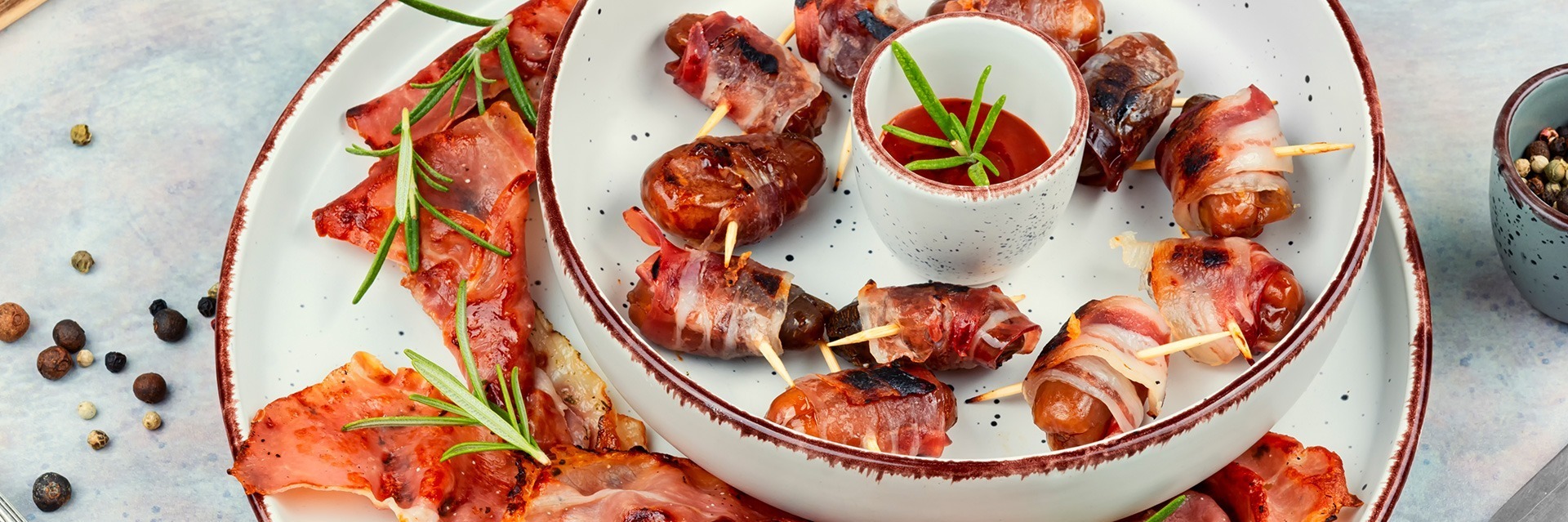 Bocaditos de salchicha a la parrilla envueltos en tocino y servidos con salsa para mojar.